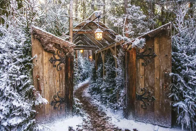 Een besneeuwd pad door een houten poort het bos in